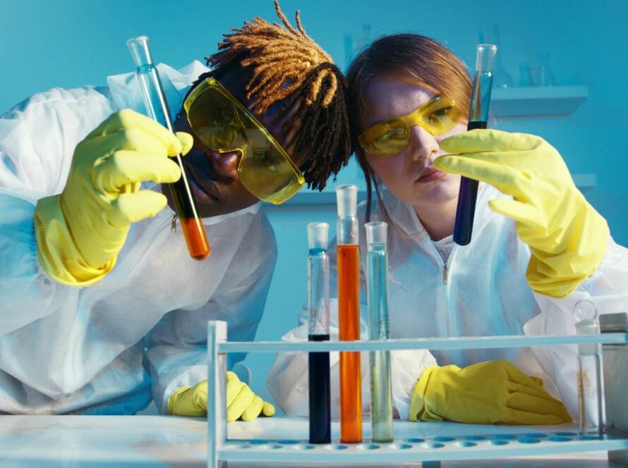 Two scientists in protective gear analyzing test tubes in a laboratory setting.