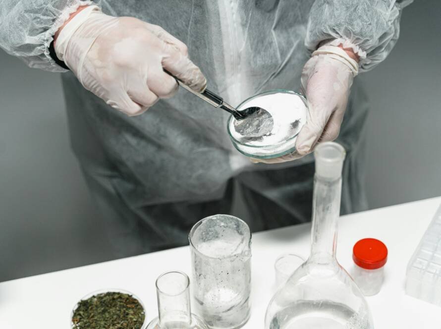 Scientist in protective gear handling powder sample in a sterile lab environment.